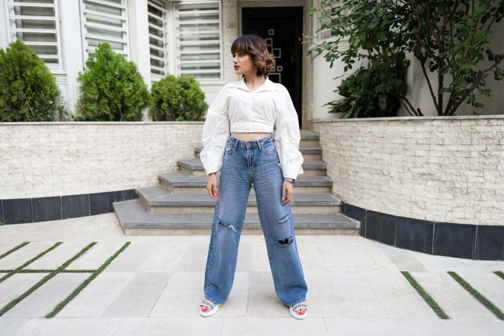 A stylish woman posing outdoors in ripped jeans and a white blouse.