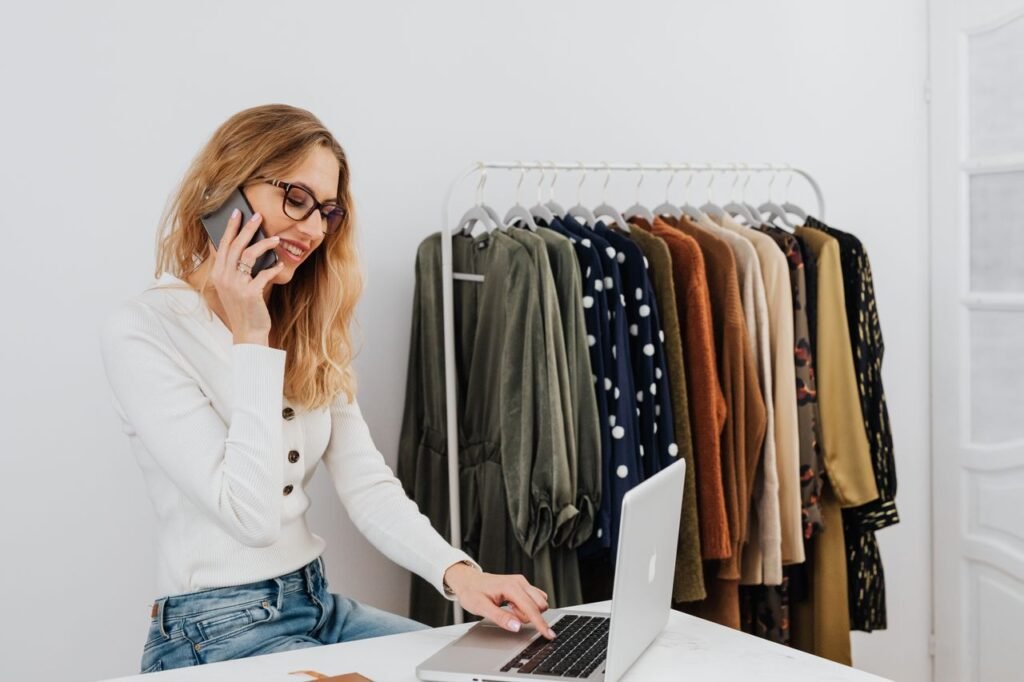 Smiling woman multitasking with phone and laptop in modern office setting.
