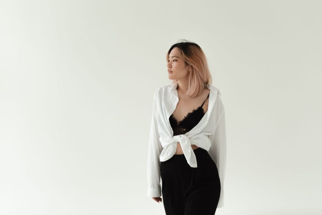 Portrait of an Asian woman in a stylish black outfit with a white blouse tied at the front, on a white studio background.